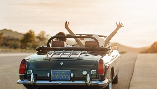 two people driving in a convertible car towards the sunset